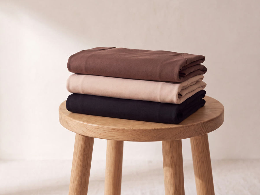 Three folded Nuuke bra tanks in mocha, nude and black stacked on a wooden stool