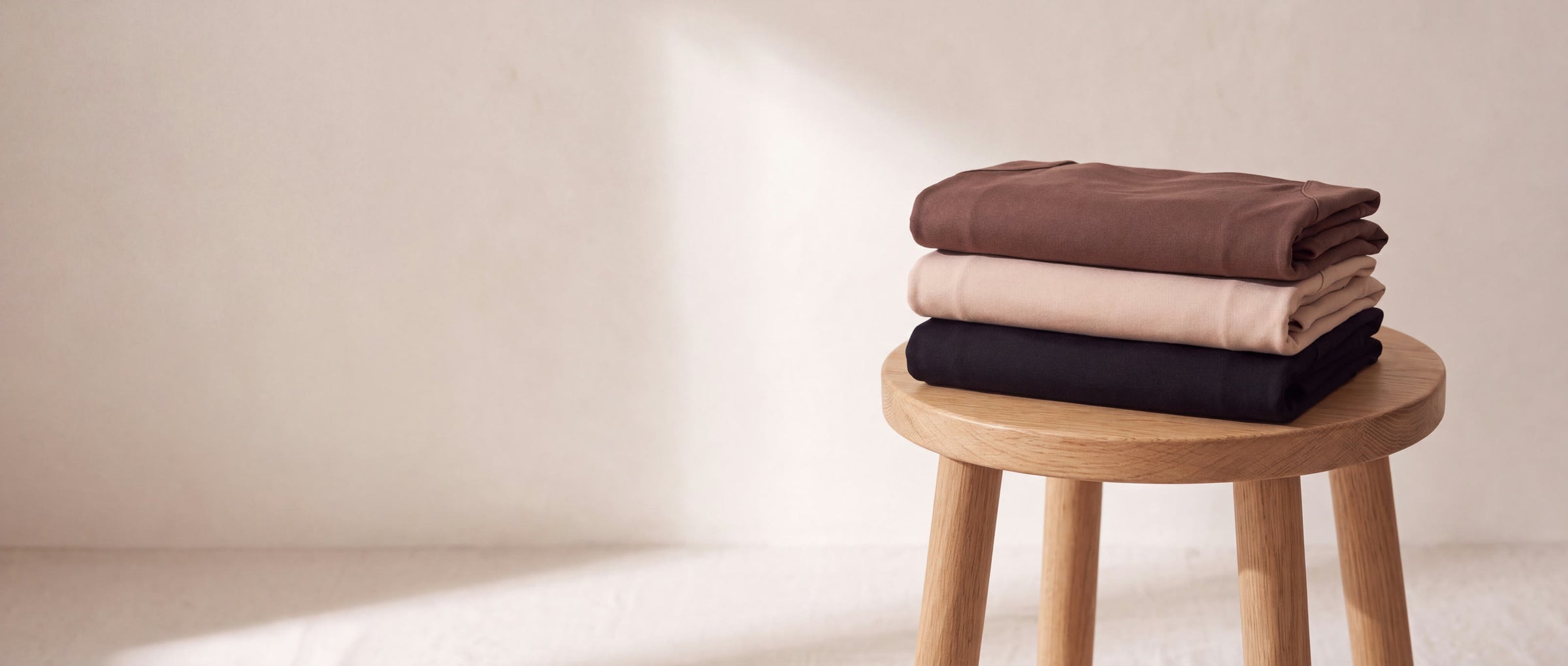 Three folded Nuuke bra tanks in mocha, nude and black stacked on a wooden stool