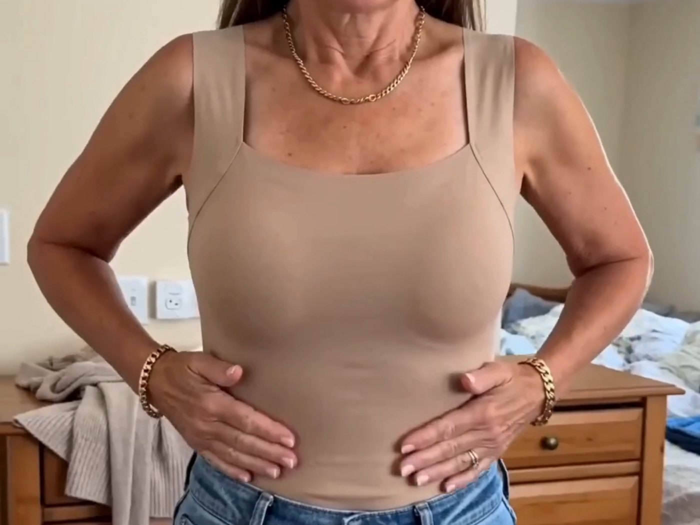Femme d’une cinquantaine d’années en débardeur à soutien-gorge intégré coloris nude, les mains sur la taille